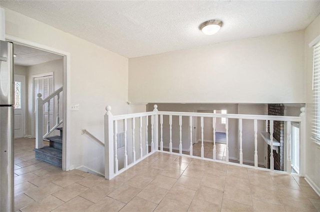 corridor with tile patterned floors, baseboards, plenty of natural light, and a textured ceiling