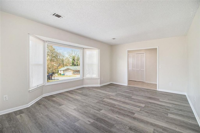 spare room with visible vents, baseboards, a textured ceiling, and wood finished floors