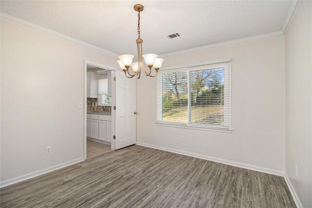 unfurnished dining area with a chandelier, visible vents, ornamental molding, and wood finished floors