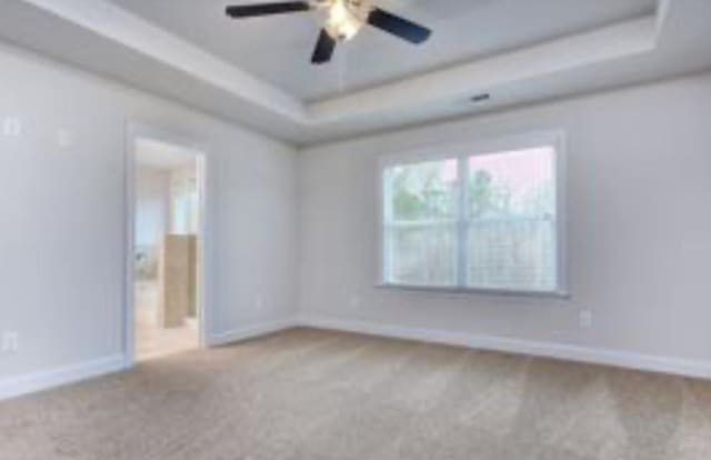 empty room featuring a raised ceiling, a ceiling fan, carpet flooring, and baseboards
