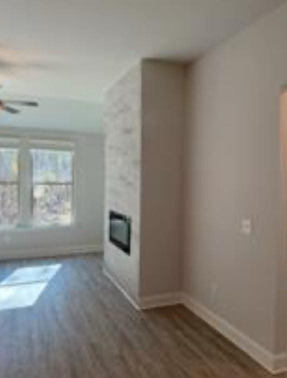 unfurnished living room featuring baseboards, wood finished floors, a ceiling fan, and a glass covered fireplace