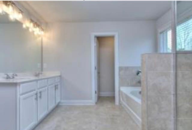 bathroom featuring baseboards, a garden tub, double vanity, and a sink