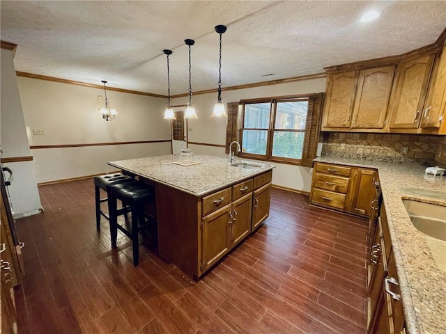 kitchen featuring an island with sink, decorative backsplash, light stone countertops, pendant lighting, and sink