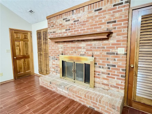 unfurnished living room with a textured ceiling, a brick fireplace, lofted ceiling, and hardwood / wood-style flooring