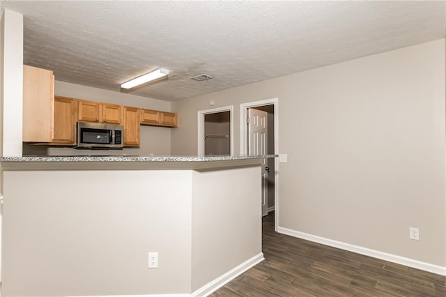 kitchen featuring a textured ceiling, kitchen peninsula, and dark hardwood / wood-style floors