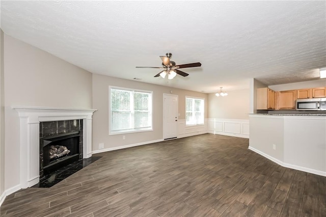 unfurnished living room featuring a textured ceiling, ceiling fan with notable chandelier, dark hardwood / wood-style floors, and a premium fireplace