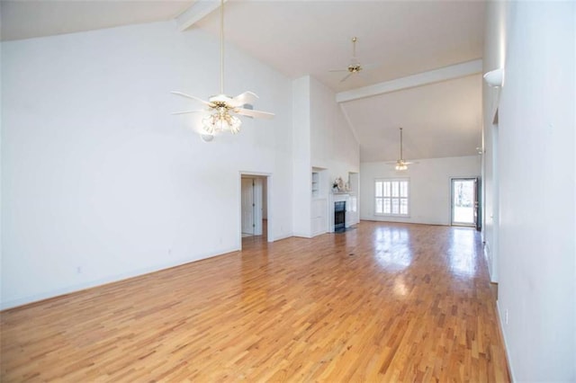unfurnished living room featuring high vaulted ceiling, light wood finished floors, beamed ceiling, ceiling fan, and a fireplace