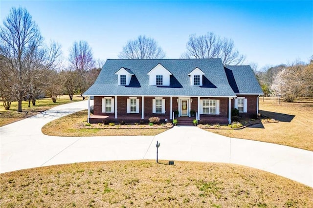 cape cod house with curved driveway, a front yard, brick siding, and covered porch
