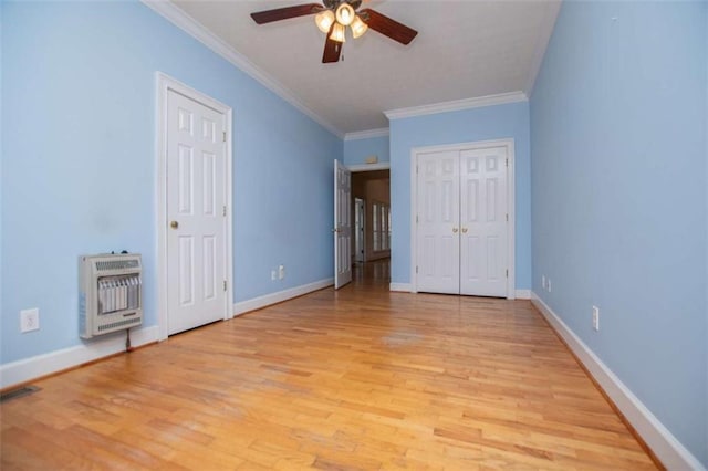 unfurnished bedroom with heating unit, light wood-style floors, ornamental molding, baseboards, and a ceiling fan