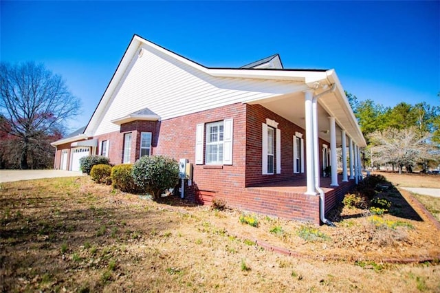 view of side of home with brick siding, covered porch, a garage, and driveway