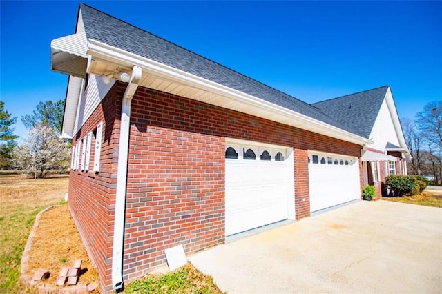 view of side of property featuring brick siding, driveway, roof with shingles, and an attached garage