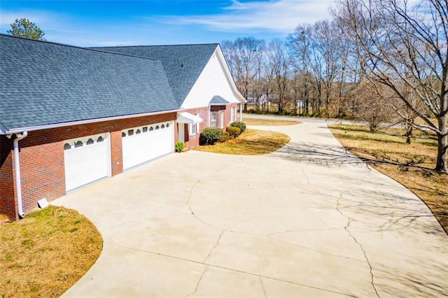 view of side of property featuring concrete driveway, a shingled roof, brick siding, and a garage