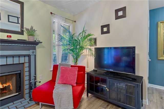 living area featuring baseboards, a lit fireplace, and wood finished floors