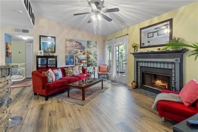 living room featuring a tiled fireplace, ceiling fan, wood finished floors, and visible vents