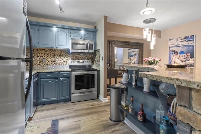kitchen with decorative backsplash, light stone counters, light wood finished floors, appliances with stainless steel finishes, and hanging light fixtures