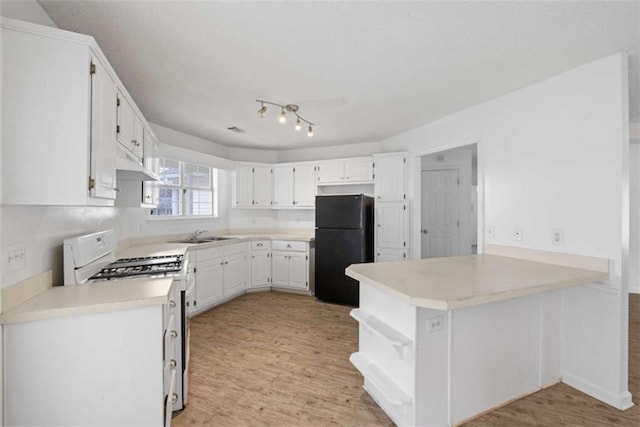 kitchen featuring white range with gas stovetop, white cabinetry, black fridge, kitchen peninsula, and light wood-type flooring