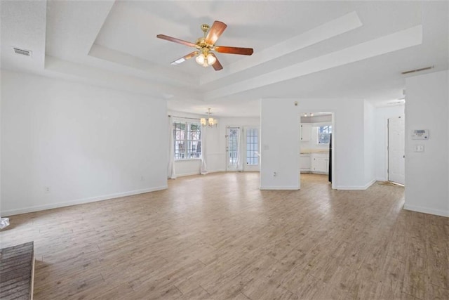 unfurnished living room featuring a raised ceiling, ceiling fan with notable chandelier, and light hardwood / wood-style flooring