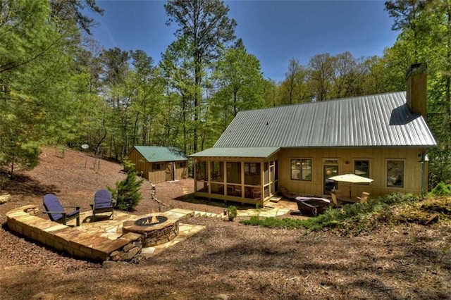 rear view of property featuring a storage shed, a sunroom, a patio, and an outdoor fire pit