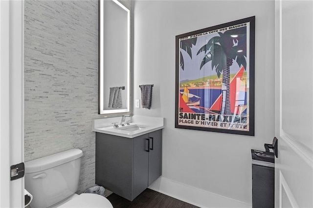 half bathroom with toilet, vanity, baseboards, and wood finished floors