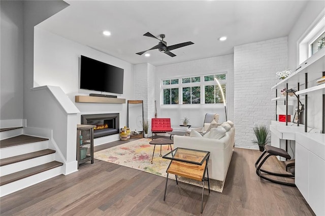 living room with a glass covered fireplace, stairs, wood finished floors, and brick wall