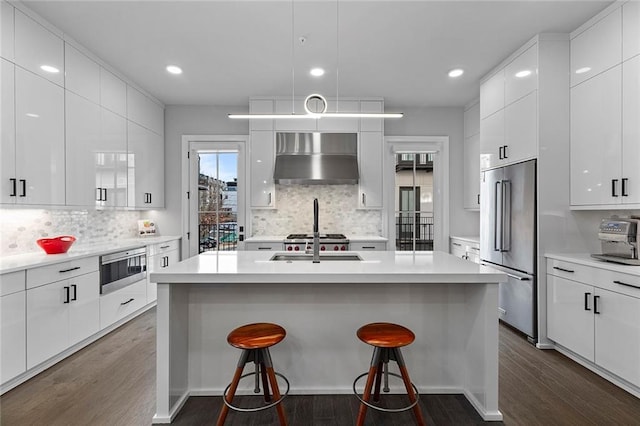 kitchen with modern cabinets, high quality fridge, a breakfast bar area, exhaust hood, and dark wood-style flooring