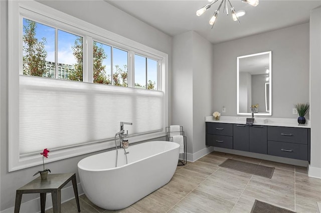 bathroom with baseboards, a soaking tub, a chandelier, and vanity