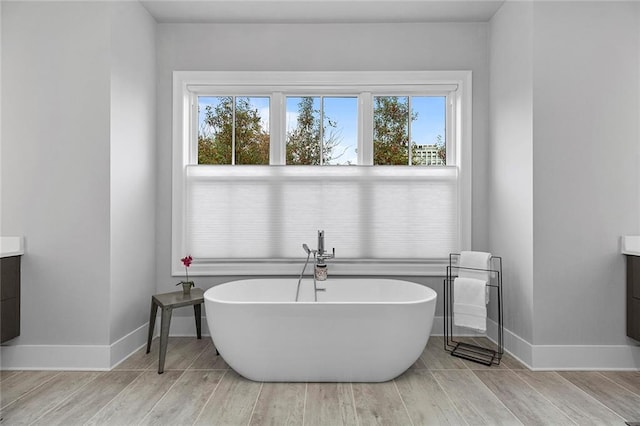 full bathroom featuring a soaking tub, vanity, and baseboards