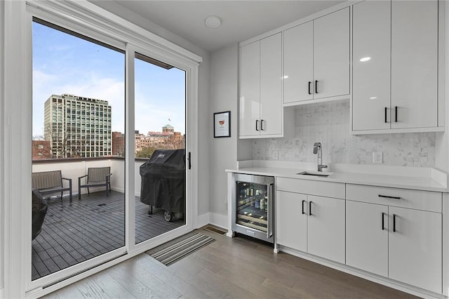 kitchen with dark wood-type flooring, beverage cooler, a sink, white cabinetry, and light countertops