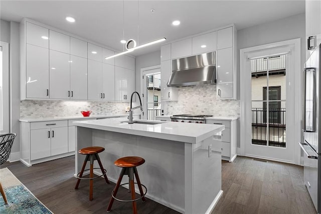 kitchen featuring high end fridge, a sink, dark wood finished floors, wall chimney exhaust hood, and light countertops