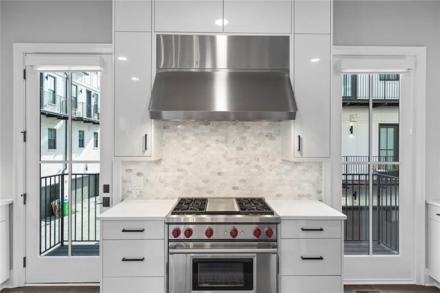 kitchen featuring backsplash, high end stove, wall chimney range hood, light countertops, and white cabinets