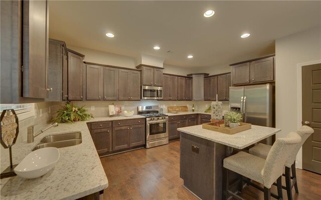 kitchen featuring a center island, sink, light stone countertops, dark hardwood / wood-style flooring, and stainless steel appliances