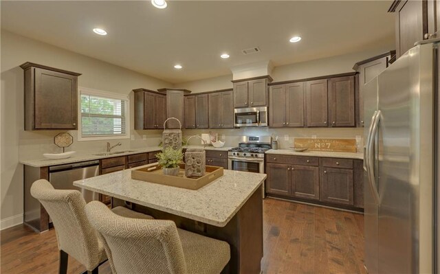 kitchen with stainless steel appliances, a kitchen breakfast bar, light stone counters, dark hardwood / wood-style flooring, and a kitchen island