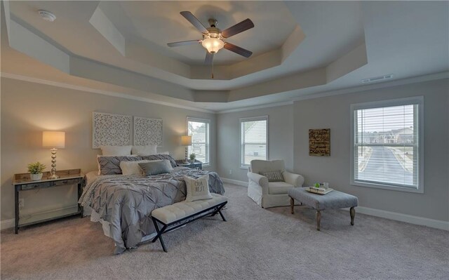 carpeted bedroom with ceiling fan, crown molding, a tray ceiling, and multiple windows