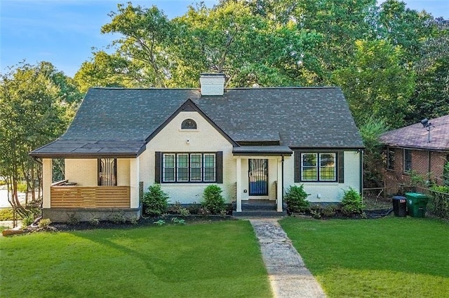 view of front facade featuring brick siding, a chimney, and a front yard