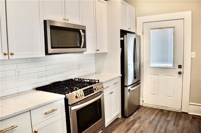 kitchen with white cabinetry, light stone countertops, backsplash, dark wood-type flooring, and appliances with stainless steel finishes