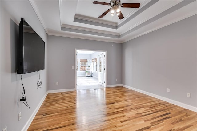 empty room with a raised ceiling, crown molding, light wood-style flooring, and baseboards