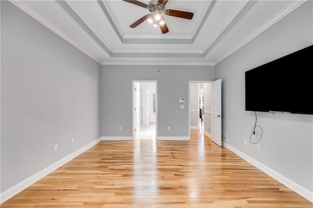 unfurnished bedroom featuring a raised ceiling, light wood-style flooring, ornamental molding, ceiling fan, and baseboards