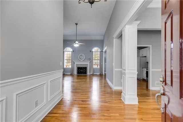 foyer entrance with ceiling fan, light wood-type flooring, a fireplace, and ornate columns