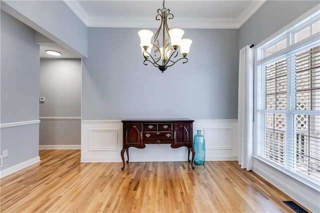 dining area featuring a chandelier, a wainscoted wall, visible vents, light wood finished floors, and crown molding