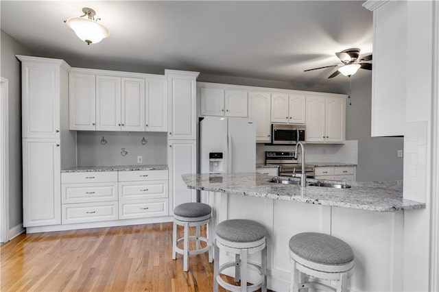 kitchen with a peninsula, white refrigerator with ice dispenser, a sink, white cabinets, and stainless steel microwave