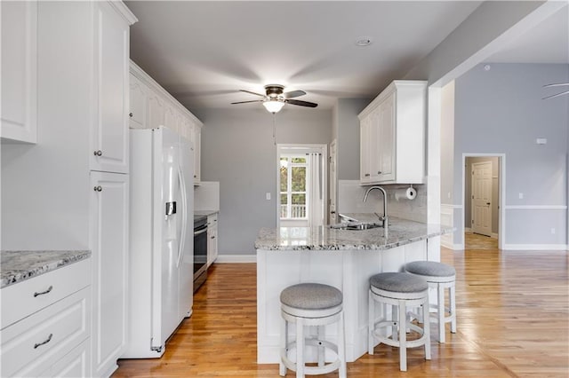 kitchen featuring ceiling fan, white refrigerator with ice dispenser, a sink, white cabinetry, and range