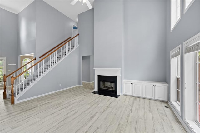 2595 Glaramara Ter, Cumming, GA 30041 - unfurnished living room with a towering ceiling, light wood-style floors, stairs, a ceiling fan, and a fireplace with flush hearth