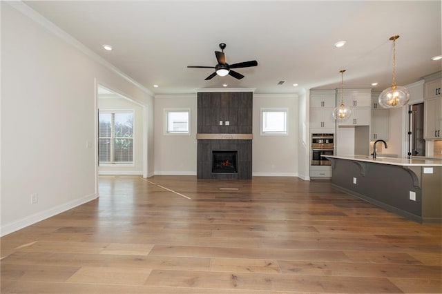 unfurnished living room with a fireplace, sink, ornamental molding, ceiling fan, and light hardwood / wood-style flooring