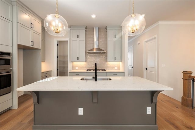 kitchen featuring decorative light fixtures, light stone countertops, wall chimney exhaust hood, and a kitchen island with sink