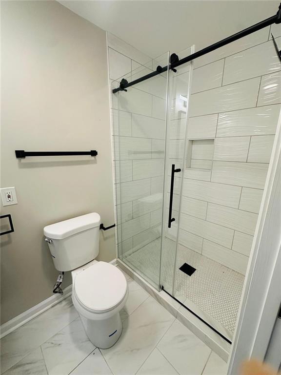 full bath with marble finish floor, a shower stall, toilet, and baseboards