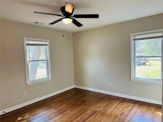 empty room with dark wood-style floors, a healthy amount of sunlight, visible vents, and baseboards