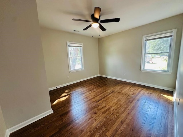 empty room with dark wood-type flooring, a healthy amount of sunlight, visible vents, and baseboards