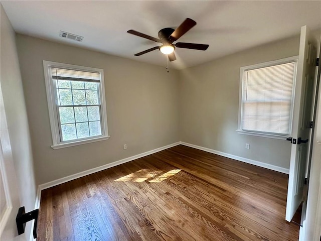 empty room featuring a ceiling fan, dark wood-style flooring, visible vents, and baseboards