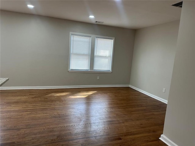 empty room featuring dark wood-style flooring, visible vents, and baseboards