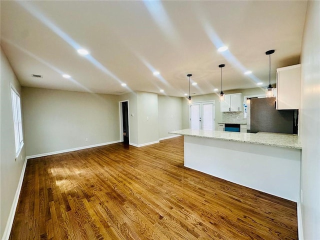 kitchen with a peninsula, wood finished floors, white cabinetry, freestanding refrigerator, and tasteful backsplash